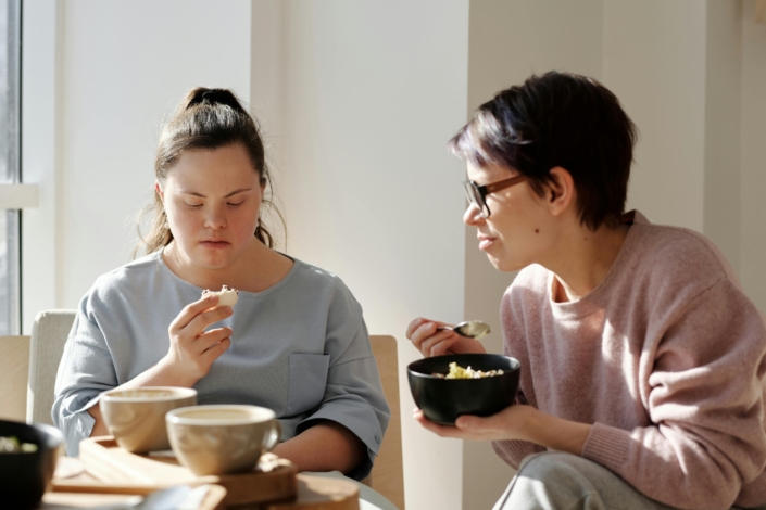 pexels-cliff-booth-4058053 a support worker sitting with a young woman eating breakfast